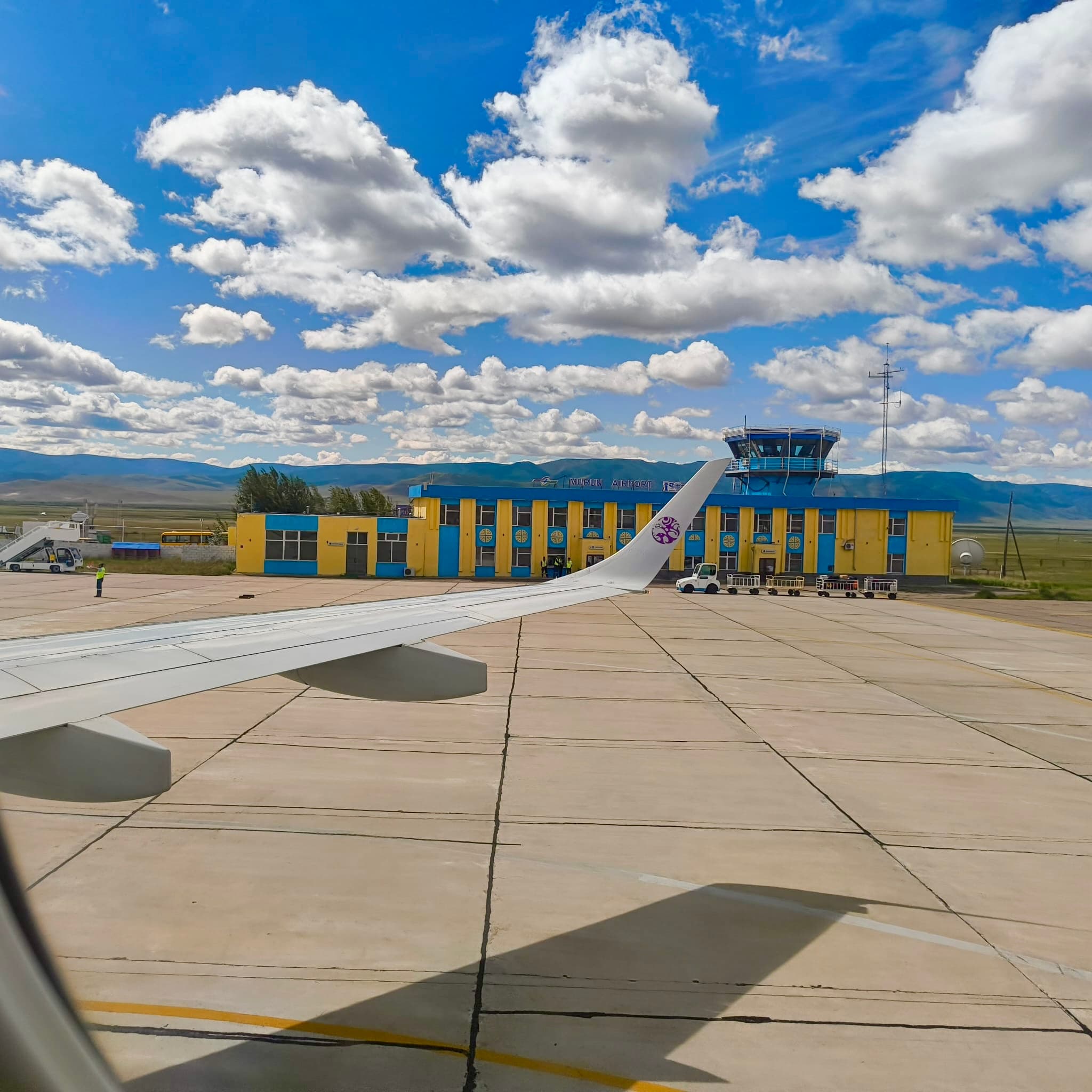 Murun Airport terminal viewed from an aircraft on the tarmac, with the wing and steppe mountains beyond.